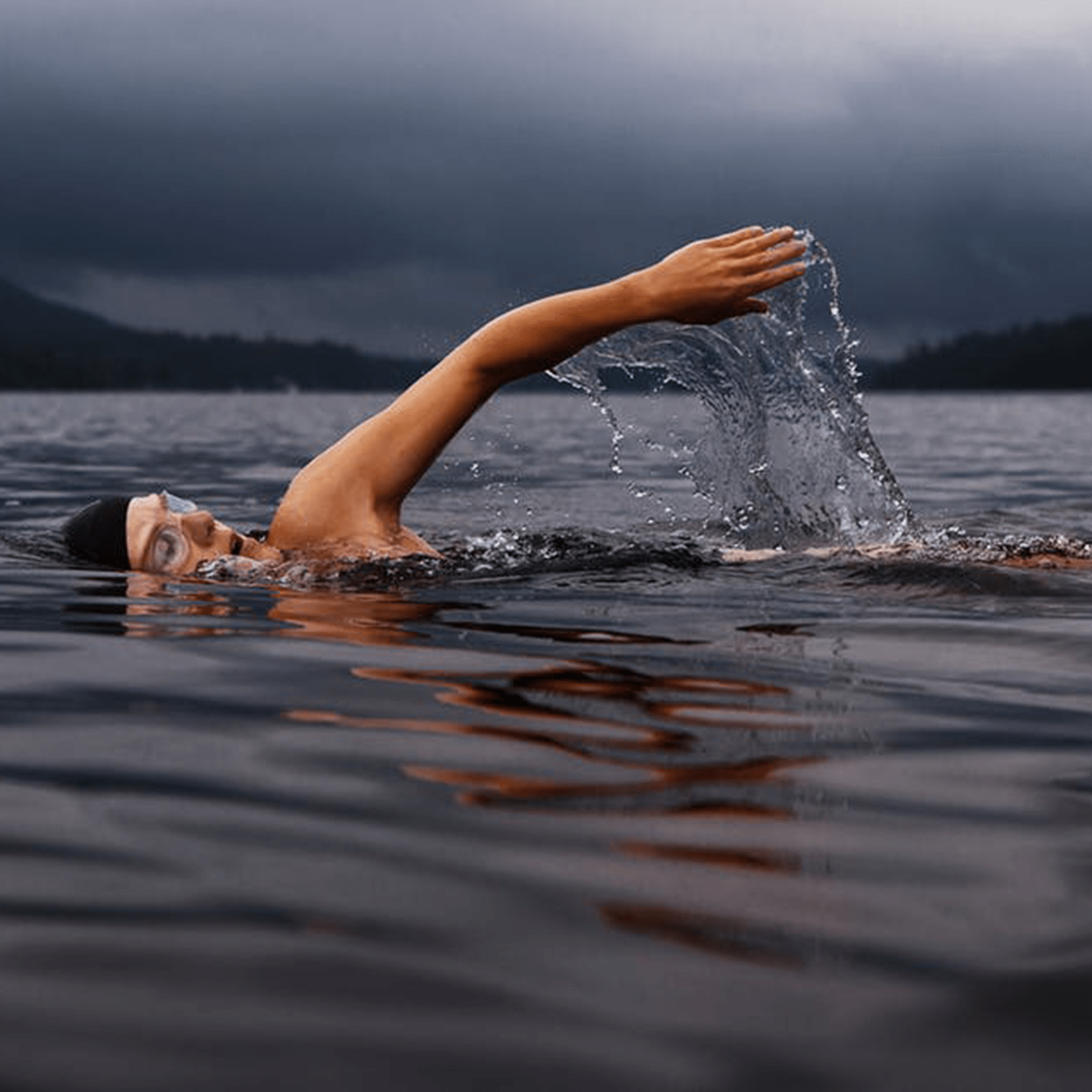 Swimmer wearing black bathing cap and goggle in a lake on a cloudy day.